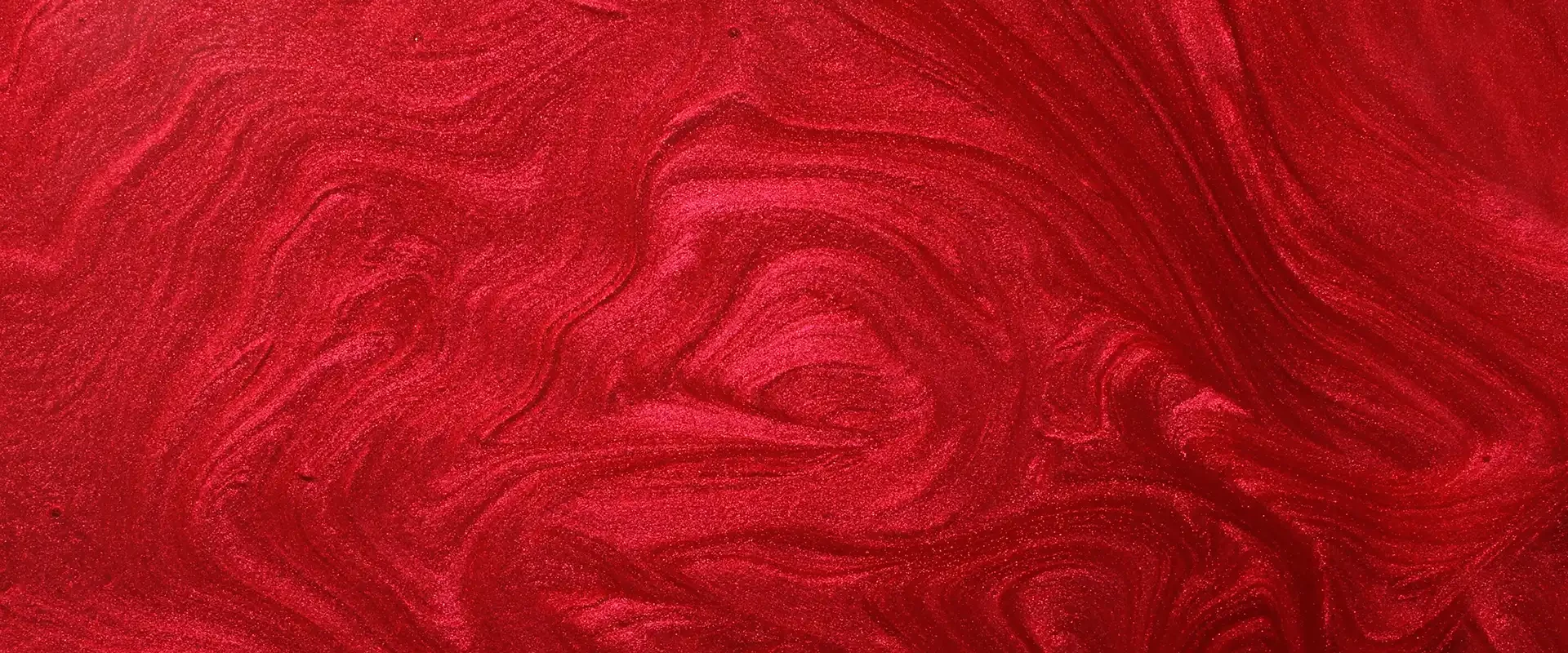 Macro view of a red shimmering lacquer surface with wavy texture and pigment swirls.