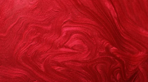 Macro view of a red shimmering lacquer surface with wavy texture and pigment swirls.