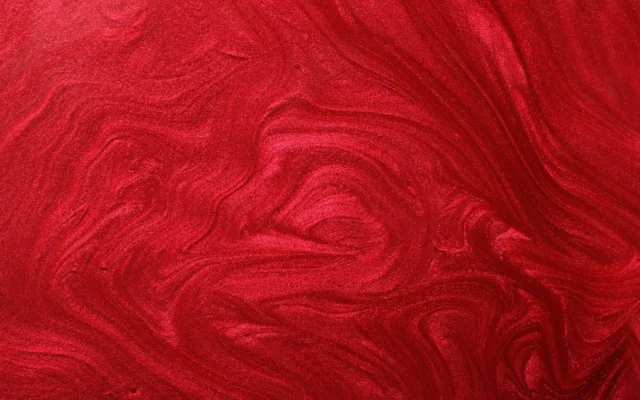 Makroaufnahme einer roten schimmernden Lackoberfläche mit welliger Struktur und Pigmentverläufen.