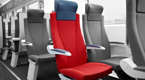 Red upholstered train seat with a blue headrest inside a carriage among grey seats.