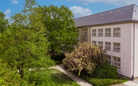 Außenansicht des EPH umgeben von Grünflächen mit blühenden Bäumen und Spazierweg.