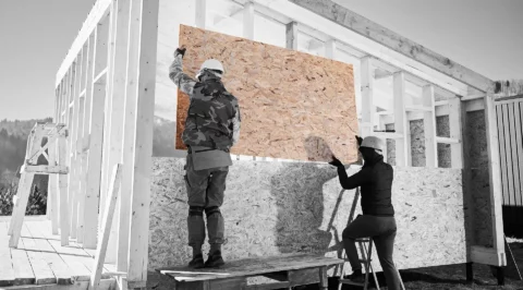 Two construction workers install an OSB as wall sheathing on a timber-frame structure