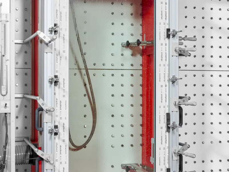 Frontansicht eines vertikalen Bewitterungsprüfstands mit Sprühwasser und Windlast in einer geschlossenen Kammer und eingespanntem Prüfrand