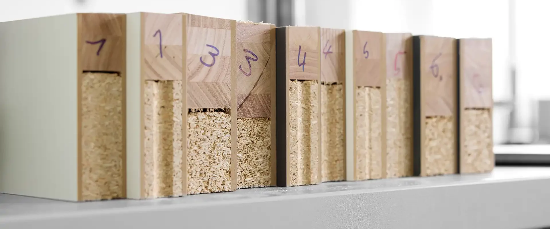 Reihe nummerierter Prüfkörper aus Holzwerkstoffen auf einem Laborregal: Querschnitte mit Spanplattenkern und unterschiedlichen Deckschichten