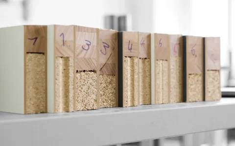 Reihe nummerierter Prüfkörper aus Holzwerkstoffen auf einem Laborregal: Querschnitte mit Spanplattenkern und unterschiedlichen Deckschichten