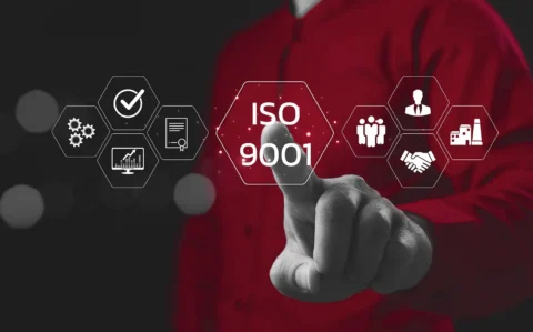 Hand tippt auf ein leuchtendes, virtuelles Sechseck mit der Aufschrift „ISO 9001“, umgeben von Icons für Qualität, Prozesse, Zertifikat, Analyse, Mitarbeitende, Führung, Partnerschaft und Produktion