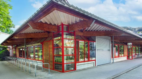 Exterior view of a single storey laboratory and office building with red framed glazing, timber cladding, wide overhang roof and bike racks.