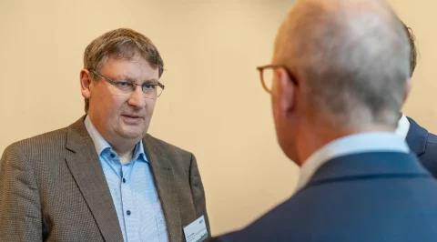 Dr Rico Emmler speaking at a meeting, another person blurred in the foreground.