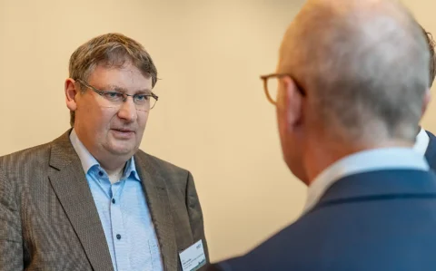 Dr. Rico Emmler spricht bei einem Treffen, eine weitere Person unscharf im Vordergrund.