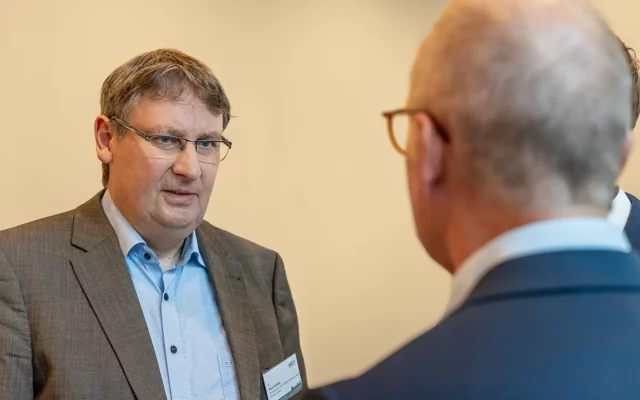 Dr. Rico Emmler spricht bei einem Treffen, eine weitere Person unscharf im Vordergrund.